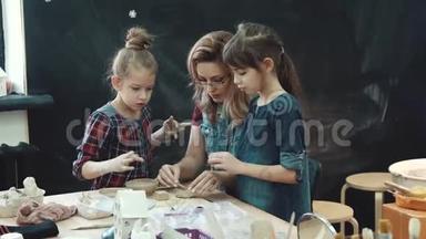 与粘土一起工作的车间。 妈妈带着两个小女儿正忙着用粘土做模特。 家长和家长的共同创造力